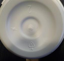 Boden der Buttermilchflasche. Weißes Plastik. 3 Symbole sind eingestanzt. Eines könnte eine 2 sein. Die beiden anderen sind nicht zuordenbar.